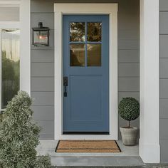 a blue front door on a gray house with two potted plants next to it