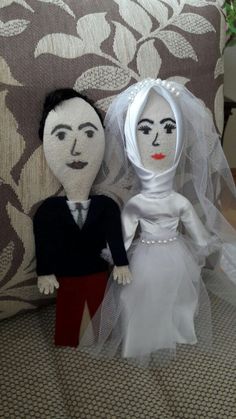 two dolls dressed up as bride and groom on a couch in front of a pillow