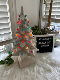 a white ceramic christmas tree sitting on top of a white fur covered floor next to a sign