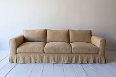 a tan couch sitting on top of a wooden floor next to a white painted wall