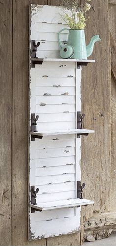 a white shelf with some flowers and a watering can on it next to a barn door