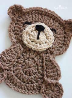 a crocheted brown teddy bear laying on top of a white table next to it's head