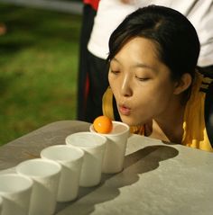 a woman is looking at an orange in a bowl on a table with other people around her