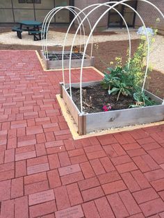 two metal planters with plants in them on a brick walkway