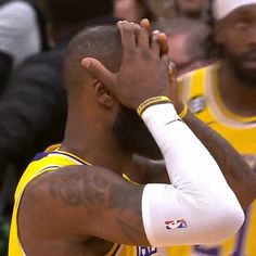 a basketball player with his hand on his head and other players in the stands behind him