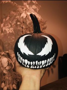 a hand holding up a black and white pumpkin with fangs on it's face