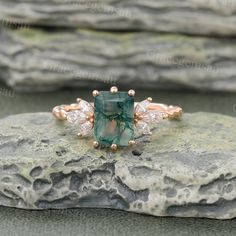 an emerald and diamond ring sitting on top of a rock