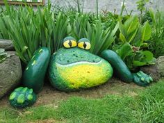 a frog statue sitting in the grass next to some rocks and plants with eyes painted on it