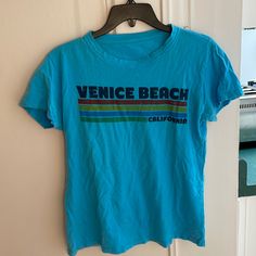 Super Cute Venice Beach T-Shirt In Preloved Condition. Tags Removed, But It Is A Size Small. Wrinkles From Storage. Very Comfortable And Cute! Too Small For Me Now Bc My Chichis Are Too Big Lol. Open To Offers! New To Poshmark? Sign Up Using My Code R_glover And Receive $10 Off Your First Purchase! Tags: Casual/Outdoor/Outside/Nwt/Nwot/Cool/Hipster/Surfer/Beach/West/Coast Blue Short Sleeve T-shirt For Beach Season, Blue Cotton T-shirt For Beach Season, Retro Style Blue T-shirt For Spring, Blue Short Sleeve Tops For Beach Season, Blue Crew Neck Tops For Beach Season, Trendy Blue Tops For Beach Season, Blue Graphic Tee For Beach, Retro Blue Top With Letter Print, Blue Short Sleeve T-shirt For Beach