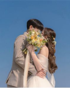 a bride and groom kissing in front of a blue sky with flowers on their forehead