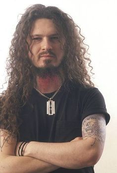 a man with long hair wearing a black t - shirt and bracelets is posing for the camera