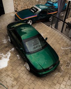 two green cars parked next to each other on a brick sidewalk in front of a building