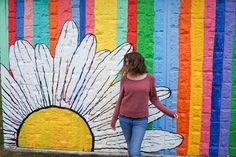 a woman standing in front of a colorful wall with a flower painted on the side