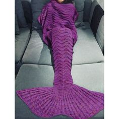 a woman laying on top of a couch covered in a purple knitted mermaid tail