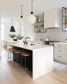 a kitchen island with stools in front of it and hanging lights above the island