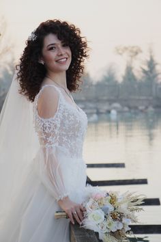 a woman in a wedding dress standing on a dock with her arms around her waist