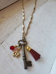 Unique, repurposed vintage skeleton key is the pendant of this necklace.  The key is a vintage skeleton key, with really cool charms attached including a burgundy suede tassle, a gold tone bow charm, and a gorgeous burgundy glass faceted bead charm.  The necklace is about 25 inches long of vintage gold metal chain, with a 3 inch extender chain, making this necklace adjustable up to 28 inches.  The key pendant is 3 inches long.  One-of-a-kind, you will love it! Old Key Necklace, Vintage Gold Necklaces With Keys, Vintage Gold Key Necklace, Antique Gold Necklaces With Two Keys, Gold Brass Necklace With Keys, Skeleton Key Crafts, Vintage Key Necklace, Key Necklace Vintage, Vintage Gold Chain