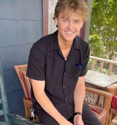 a smiling man sitting on a chair outside