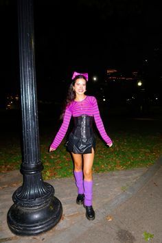 a woman in pink shirt and black skirt standing next to a lamp post at night