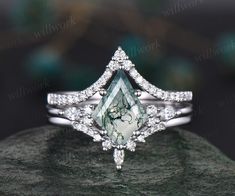 an engagement ring with a pear shaped green diamond surrounded by white diamonds on top of a rock