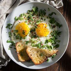 two fried eggs are on top of toast and lettuce in a white bowl