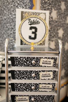 the table number is placed on top of some black and white boxes with gold trim