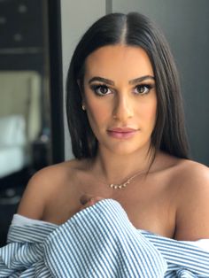 a woman with long dark hair wearing a blue and white stripped shirt is looking at the camera