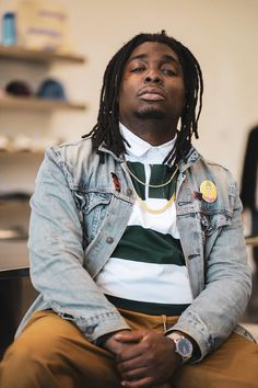 a man with dreadlocks sitting in front of a counter wearing a jean jacket