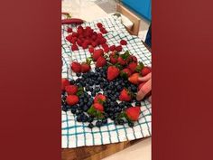 someone is cutting strawberries and blueberries on a table with a checkered cloth