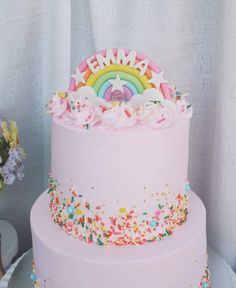 a pink cake with sprinkles and a rainbow on top