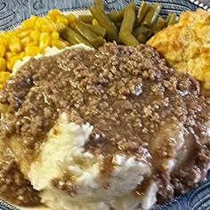 a blue plate topped with mashed potatoes, green beans and other foods next to corn