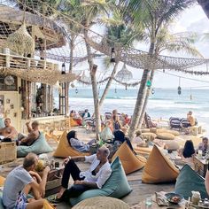 people sitting on bean bag chairs at the beach with palm trees in the foreground