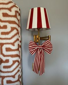 a red and white striped lamp next to a wall hanging with a bow on it