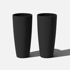 two tall black cups sitting next to each other on a white surface with shadow from the floor