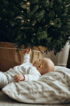 a baby is laying on the floor under a christmas tree and looking up at it