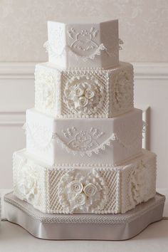 a three tiered wedding cake with white lace and flowers on the top, sitting on a table