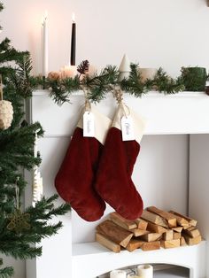 two christmas stockings hanging from a mantel with candles and logs in front of them