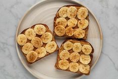 three slices of toast with banana slices on them sitting on a white plate next to a marble countertop