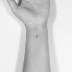 a small tattoo on the wrist of a woman's arm, with a bird flying above it