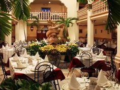 an indoor dining area with tables, chairs and potted plants on the table in front of a fountain