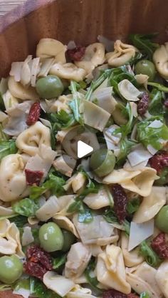 a wooden bowl filled with pasta salad and green olives on top of a table