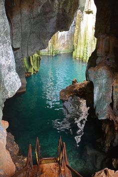 stairs lead down to the water in an underground cave with blue waters and green cliffs