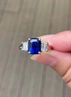 a woman's hand holding an engagement ring with blue sapphire and diamond sidestones