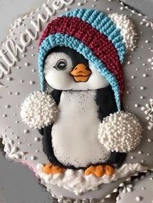 a decorated cake with a penguin wearing a knitted hat