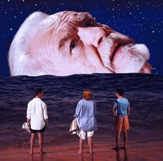 three people standing on the beach looking at an image of a man's face