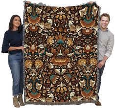 a man and woman holding up a large tapestry with an ornate design on the front