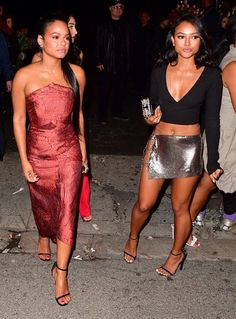 two women are walking down the street at night, one is wearing a black top and silver skirt