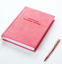 a pink book with writing on it next to a pen