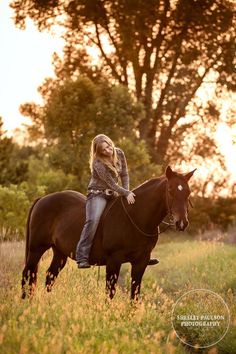 a woman riding on the back of a brown horse in a grassy field at sunset