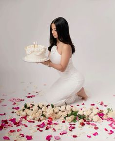 a woman kneeling down with a cake on a plate in front of flowers and petals